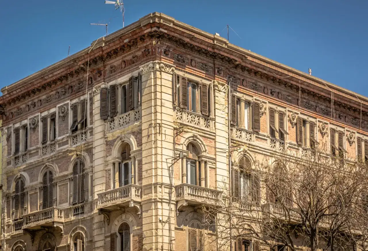 Angolo del **Palazzo Accardo a Cagliari**, con facciata in pietra chiara, balconi in ferro battuto e finestre con persiane.