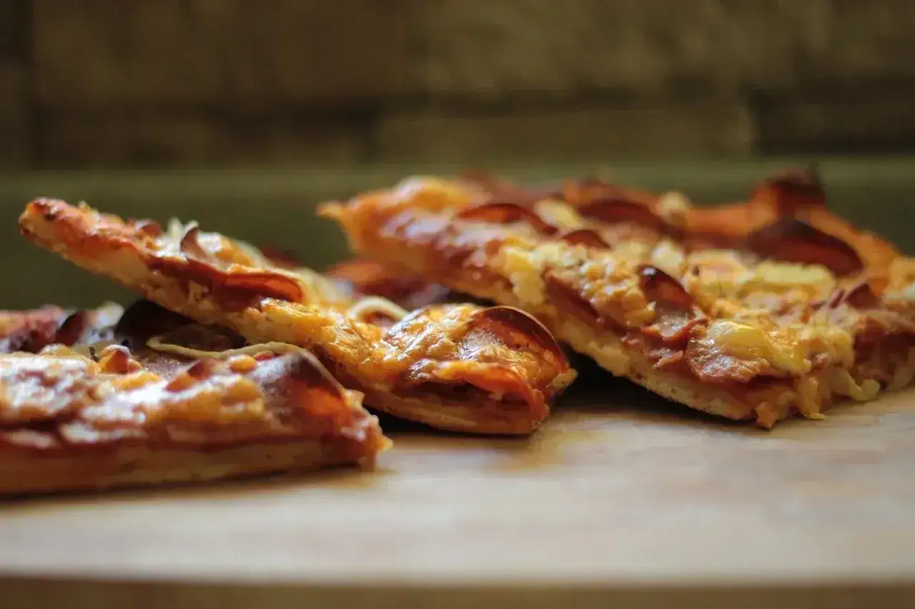 Kawałki pysznej, domowej pizza polska z serem i kiełbasą, apetycznie wyglądające na drewnianym blacie.