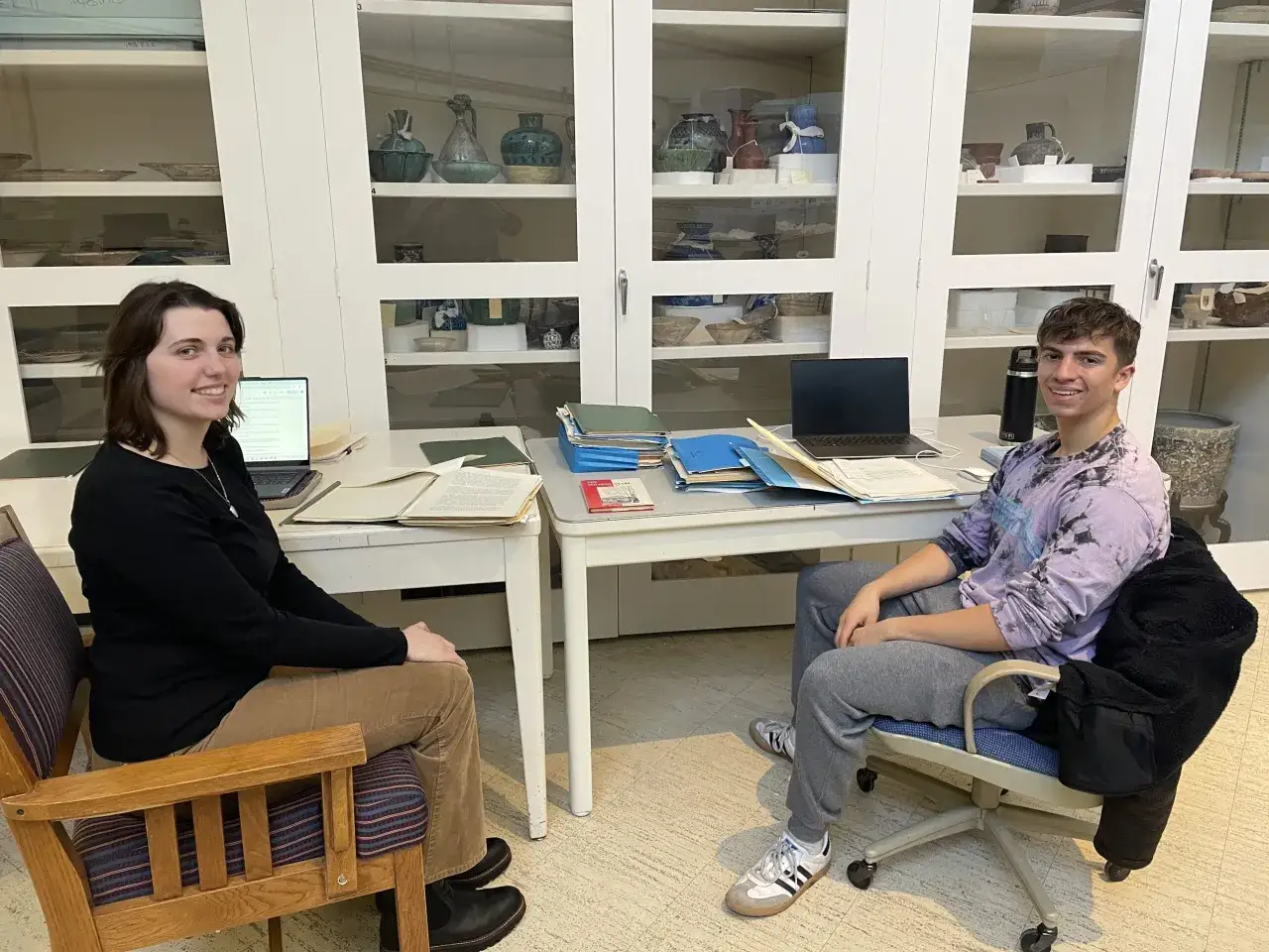 Two students study in a museum archive, surrounded by artifacts. This is a great setting for anyone pursuing best art history graduate programs.