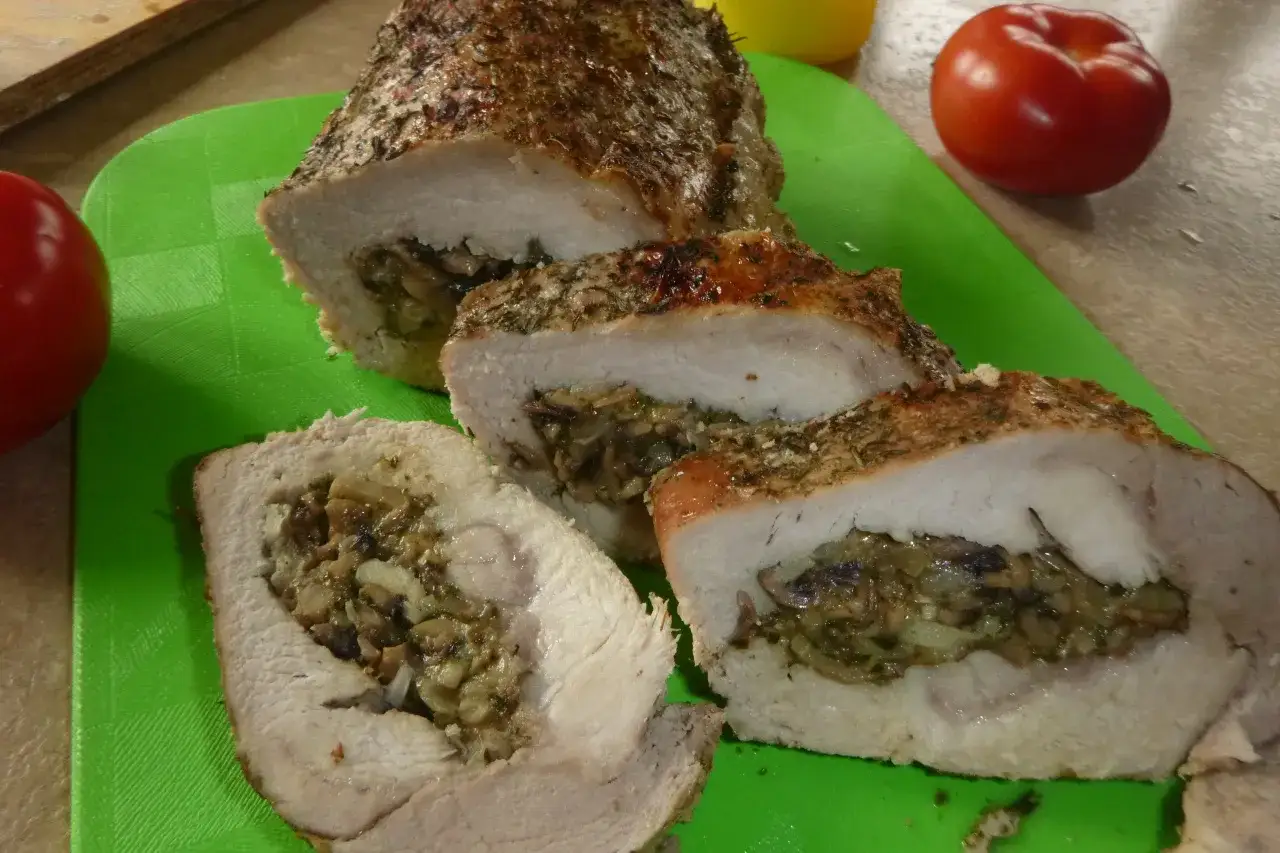 Pyszny kotlet husarski, pieczony z ziołami i nadzieniem grzybowym, pokrojony na plastry. Obok pomidory.