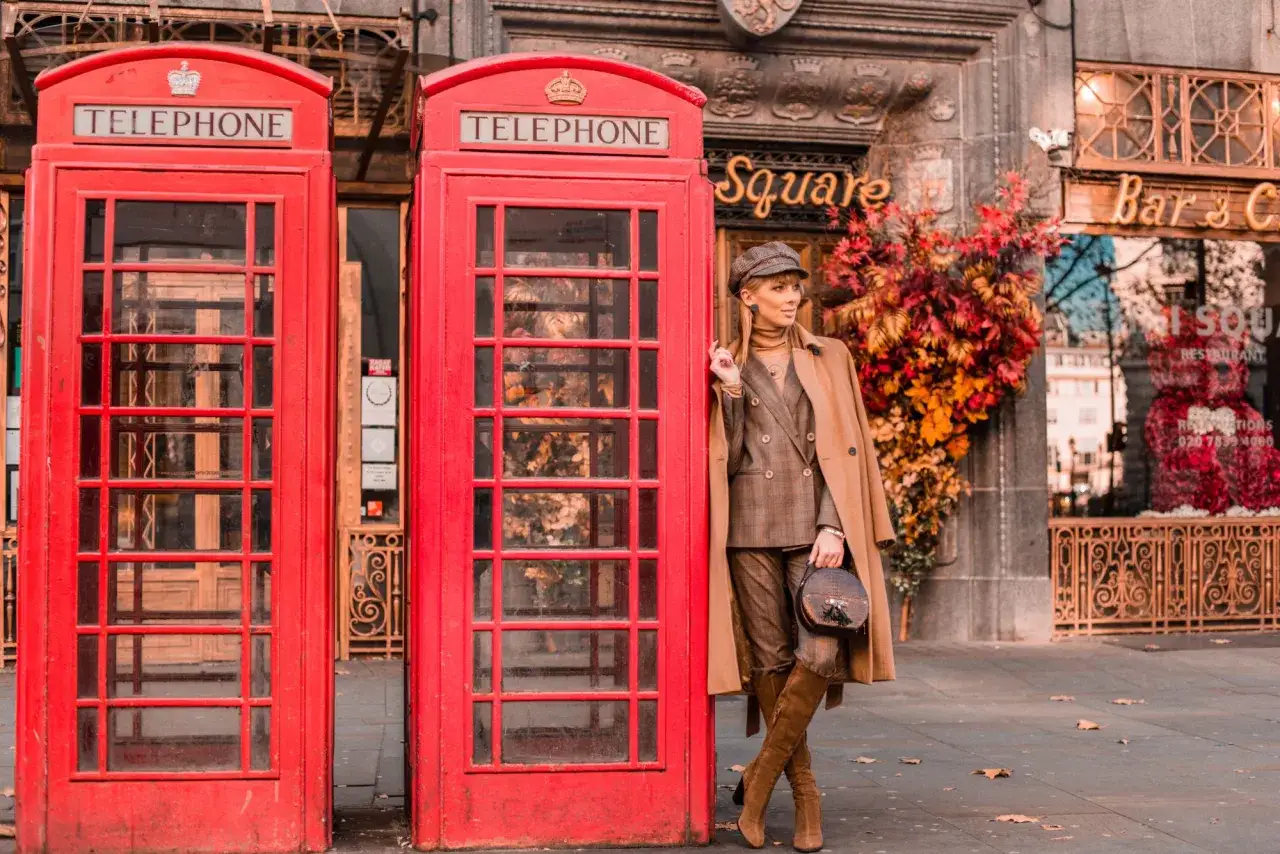 Elegancka kobieta w płaszczu i garniturze pozuje przy czerwonej budce telefonicznej, tworząc klasyczny london look.