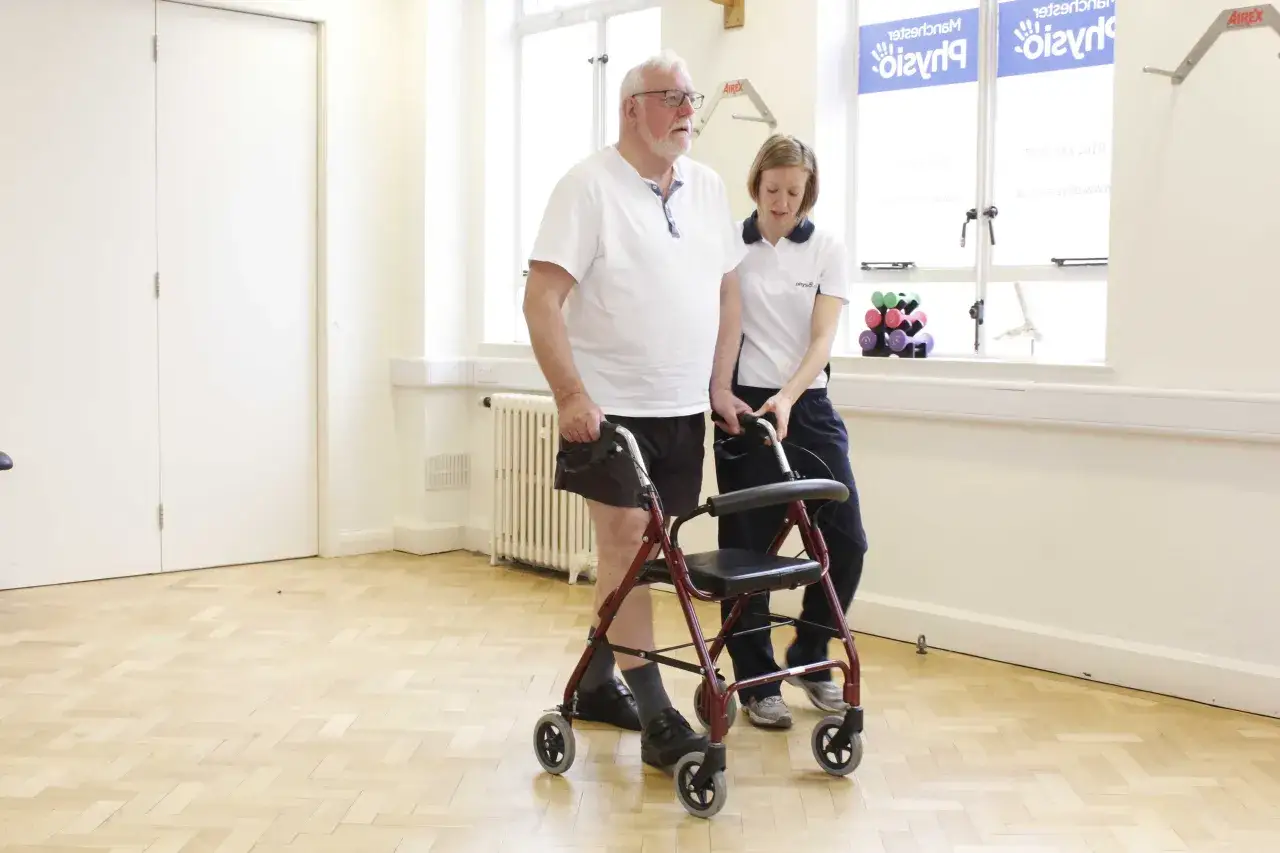 Ein &auml;lterer Mann mit Gehhilfe wird von einer Physiotherapeutin unterst&uuml;tzt. M&ouml;gliche Enzephalopathie-Symptome erfordern oft solche Hilfen.