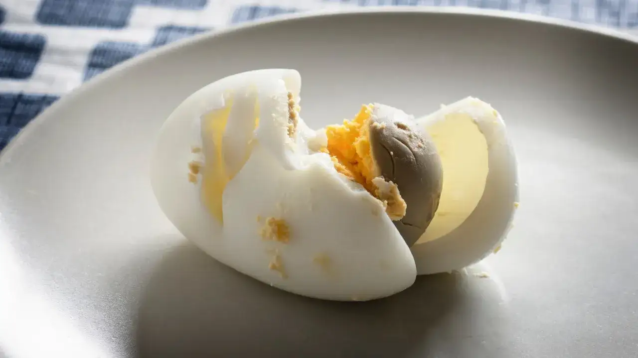 Un œuf trop cuit, coupé en deux, révèle un jaune grisâtre et sec. La texture pâteuse témoigne d'une cuisson prolongée.