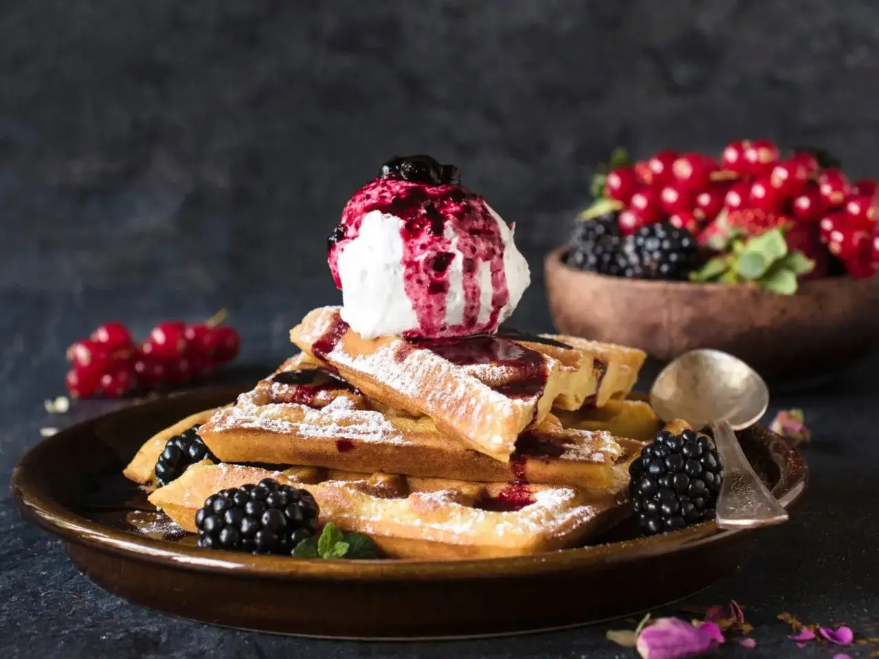 Ein Stapel goldbrauner Waffeln, bestäubt mit Puderzucker, garniert mit Sahne und Beerensoße. Ein köstliches Waffeln Rezept für den Genuss.