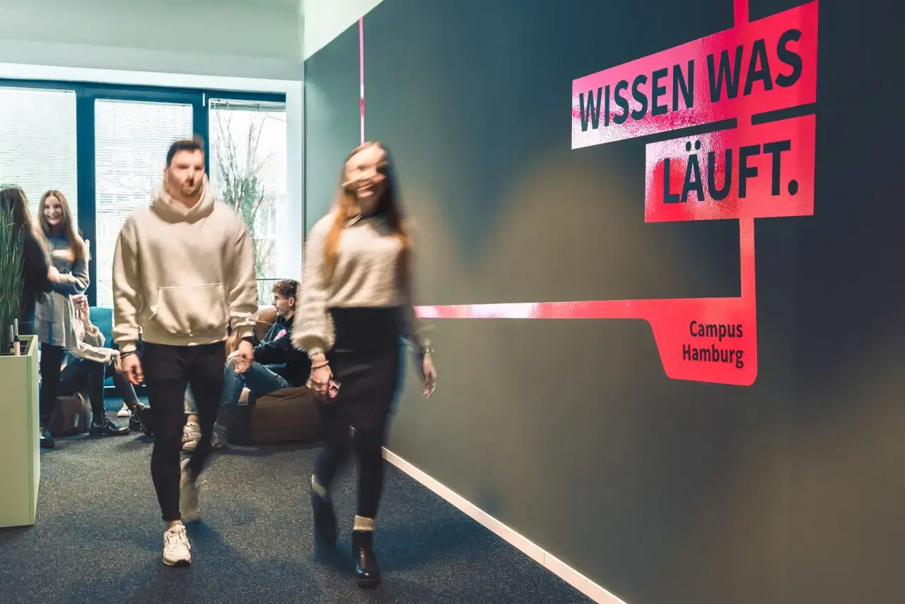 Menschen bewegen sich in einem modernen Flur, wo kollaboratives Arbeiten im Fokus steht. Ein Schild mit der Aufschrift 