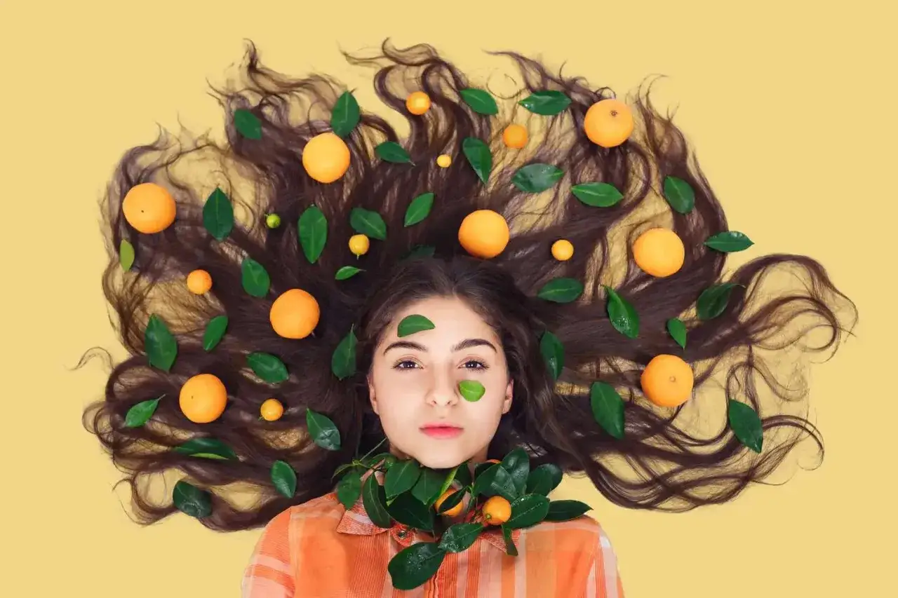 Capelli lunghi e scuri adornati da arance e foglie verdi, un'esplosione di vitamina C per capelli luminosi e sani.