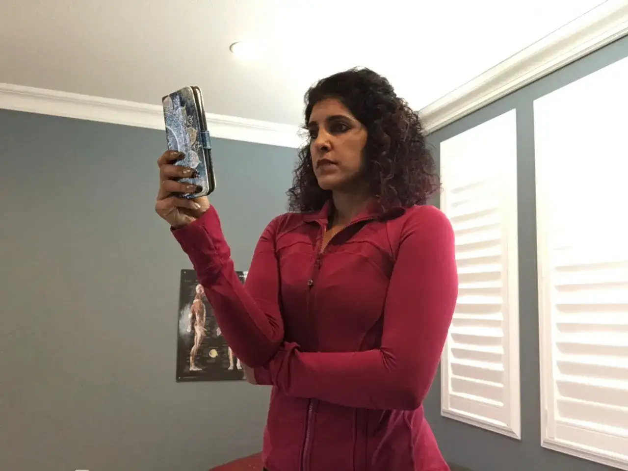 Donna con capelli ricci guarda il suo telefono, con una postura che potrebbe causare il 