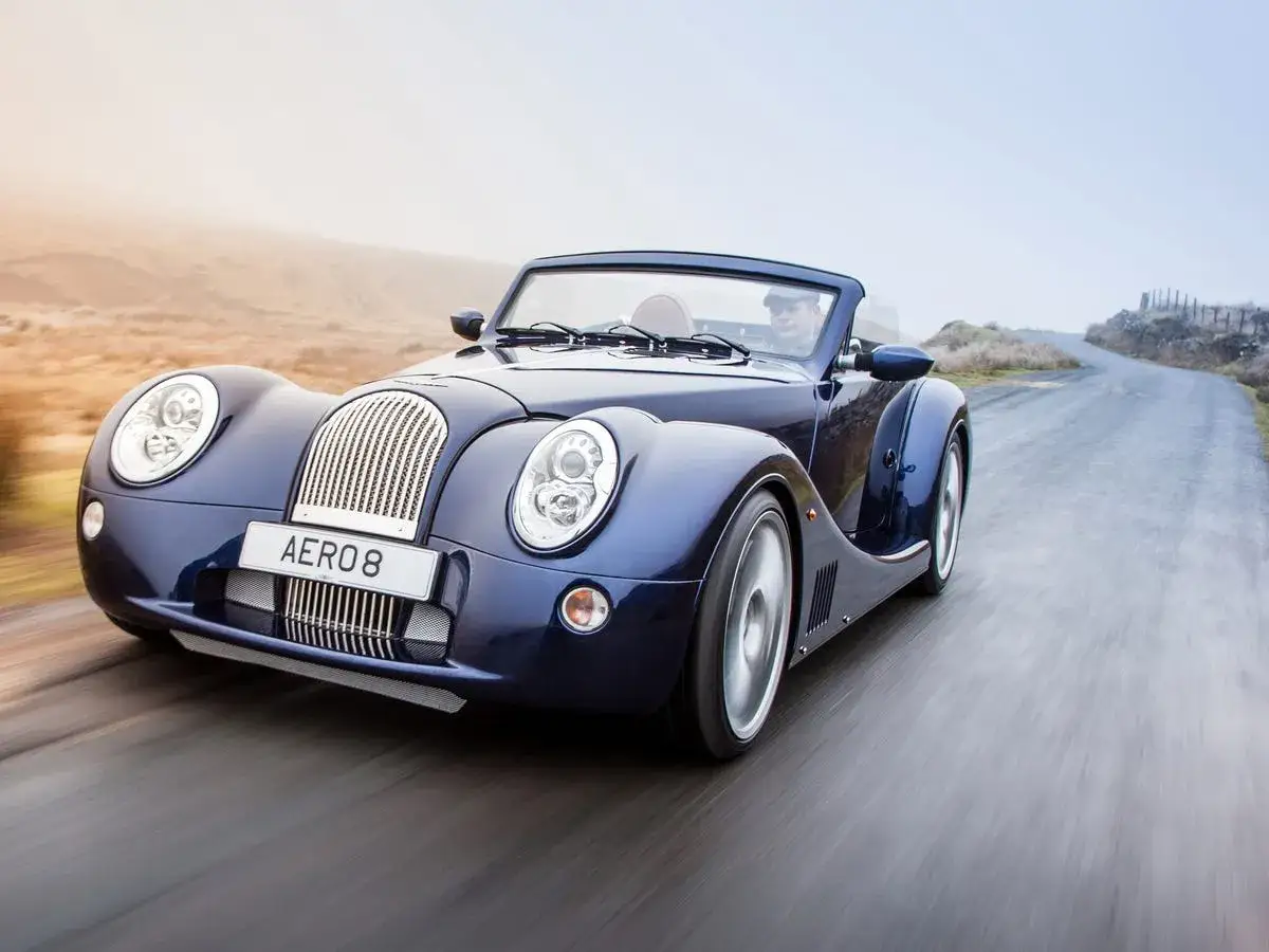 Niebieski Morgan Aero 8, jeden z tych kanciastych samochodów, pędzi po krętej drodze.