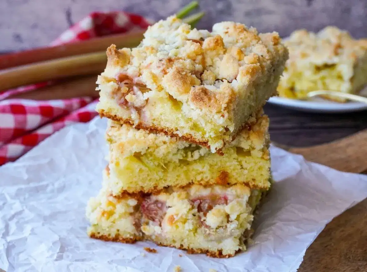 Saftiger rhabarberkuchen mit Streuseln, gestapelt auf weißem Papier. Ein köstlicher Genuss für den Nachmittagstee.