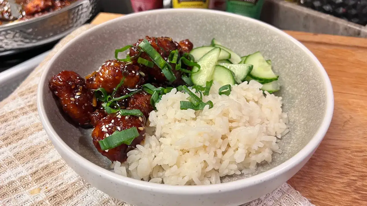En skål med kyckling och ris, toppad med gurka och salladslök. En läcker måltid!