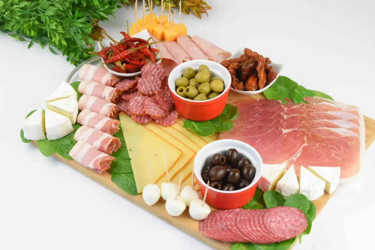 Patera wędlin i serów: salami, szynka, prosciutto, sery, oliwki, suszone pomidory i papryczki chili.
