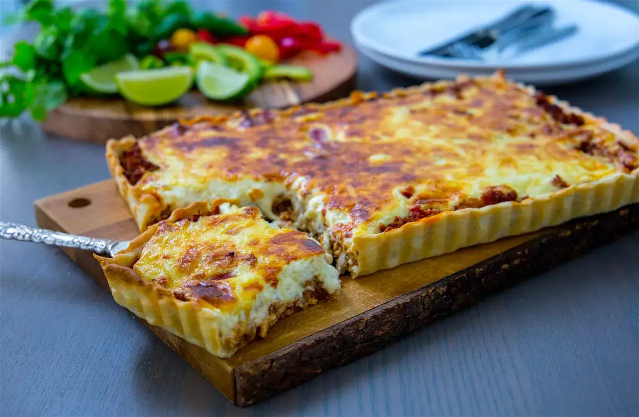En gyllene tacopaj i långpanna, redo att serveras. En bit är uppskuren och visar den smakrika fyllningen.