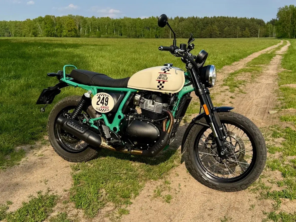 Customowy Royal Enfield Himalayan z numerem 249 na tle zielonej łąki i lasu.