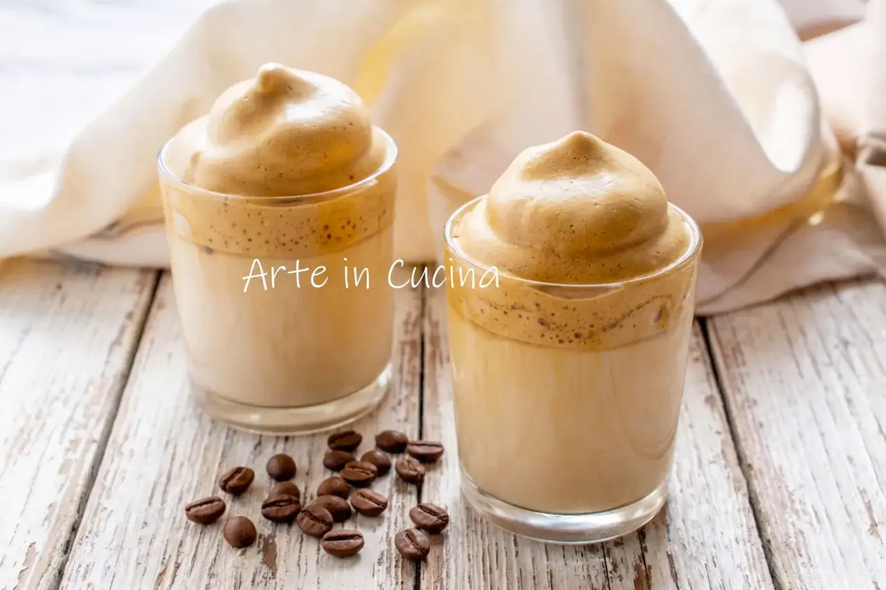 Due bicchieri di spumone al caff&egrave;, con la schiuma densa e cremosa che corona il latte. Chicchi di caff&egrave; tostati sparsi sul tavolo di legno.