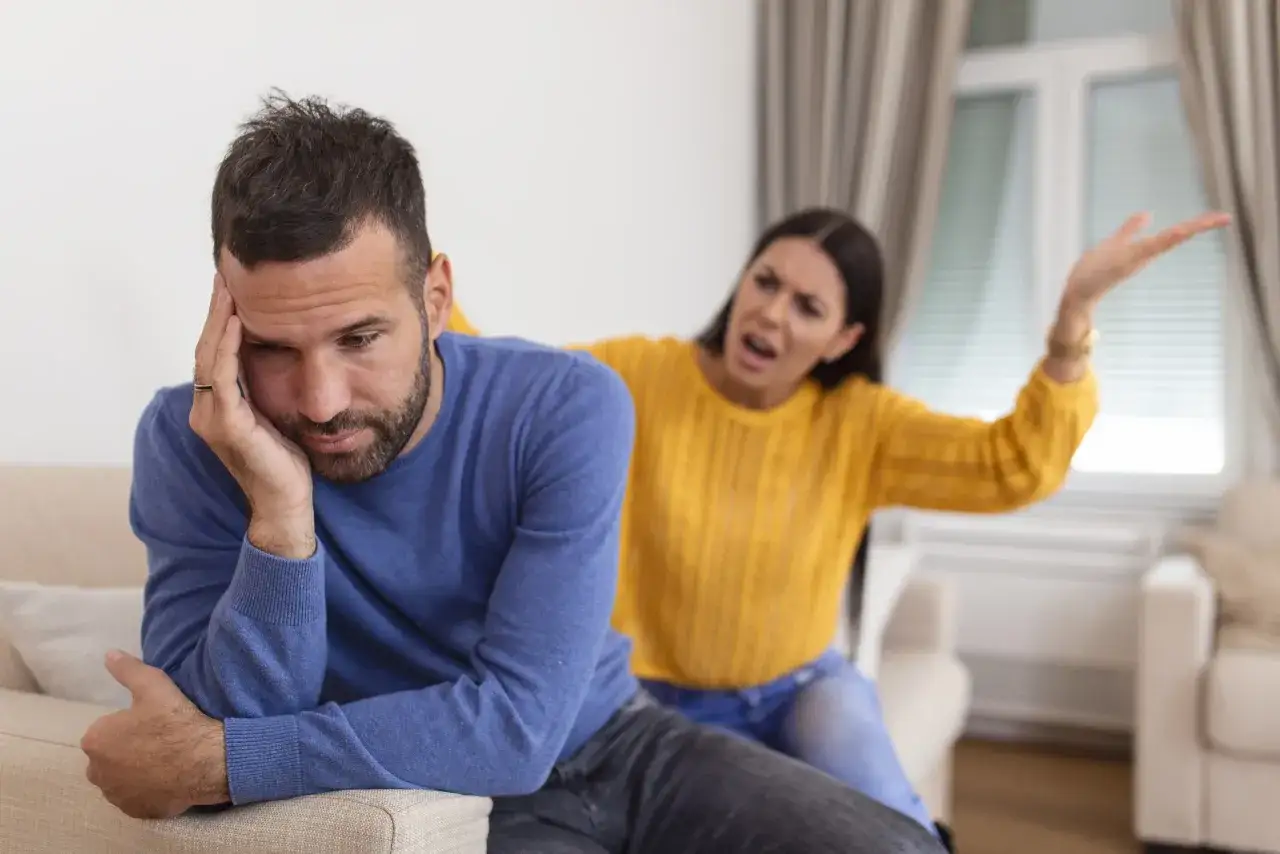 Un homme fatigu&eacute; se tient la t&ecirc;te, tandis qu'une femme en col&egrave;re lui crie dessus. Une sc&egrave;ne typique de la crise des 1 an d'un couple.