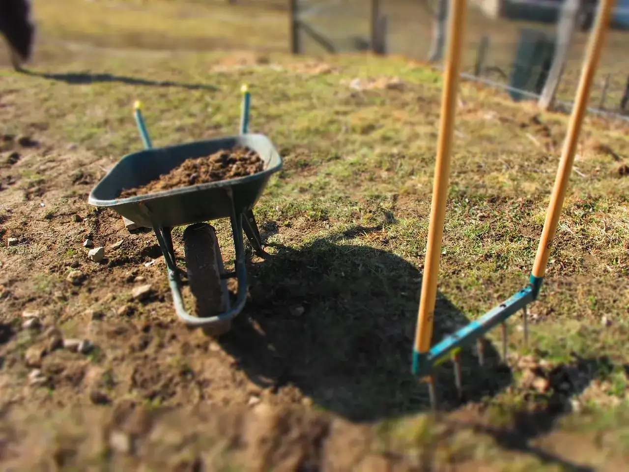 Brouette remplie de terre dure comme de la pierre, à côté d'un râteau prêt pour le jardinage.