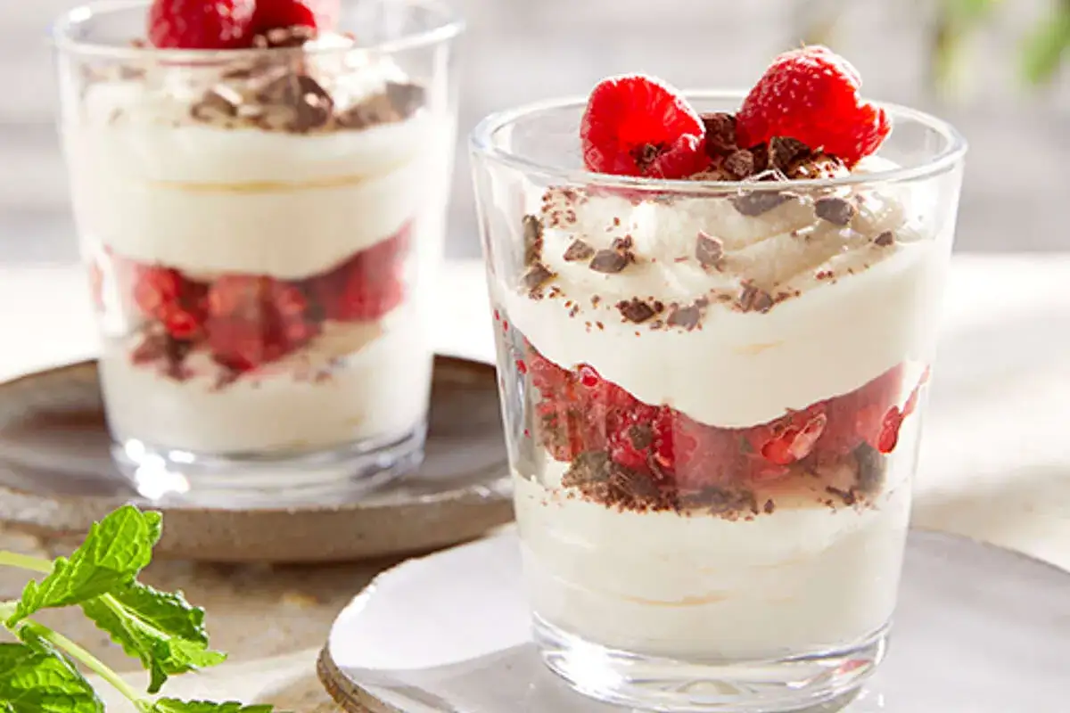 D&eacute;licieuse mousse chocolat blanc et framboises, superpos&eacute;es dans un verre, garnie de fruits rouges et de copeaux de chocolat.
