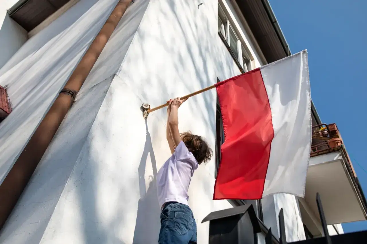 Dziecko wiesza biało-czerwoną flagę polską na ścianie domu. Duma narodowa w słoneczny dzień.