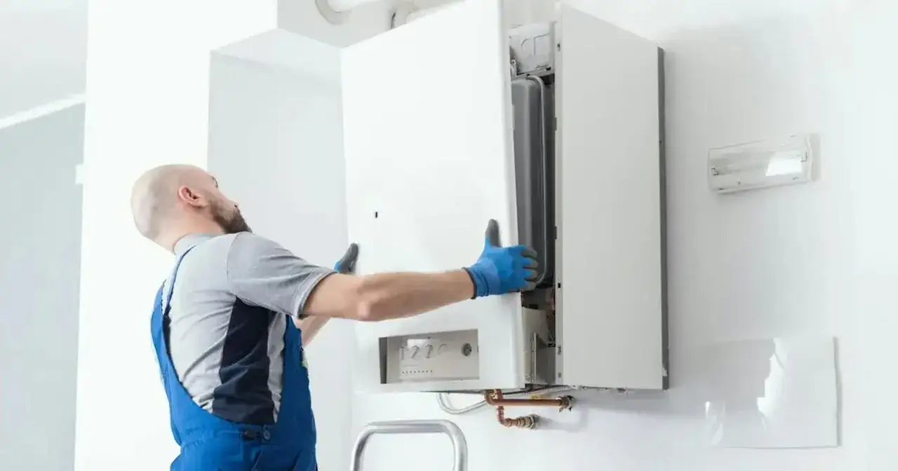 Un technicien en bleu manipule une chaudière blanche. Le propriétaire ne veut pas changer chaudière, mais le technicien inspecte l'appareil.