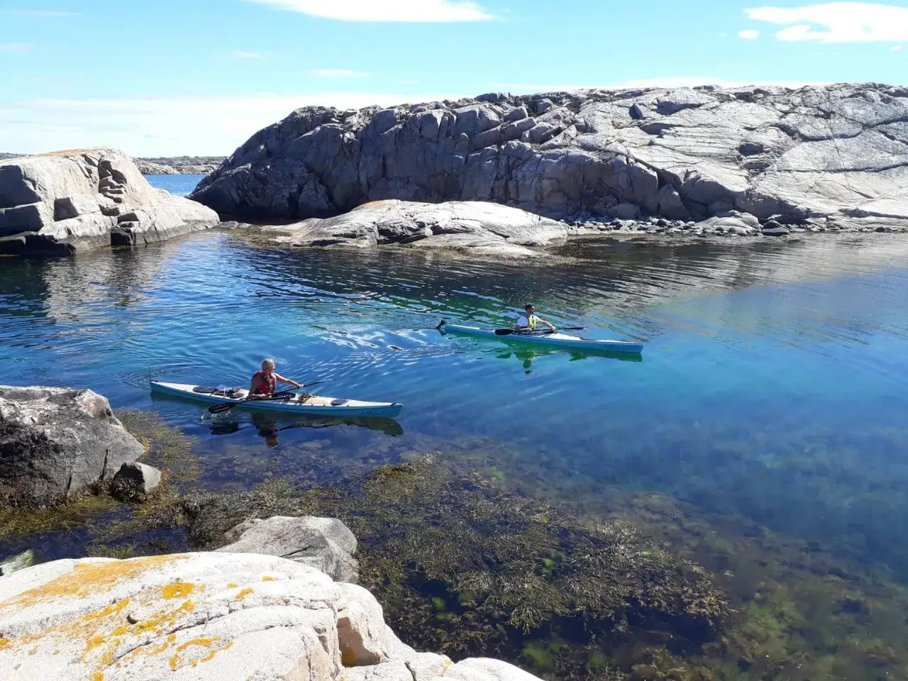 Två personer paddlar kajak i klart, blått vatten mellan klippor. En fråga som dyker upp är hur långt paddlar man på en dag i sådana vackra omgivningar.