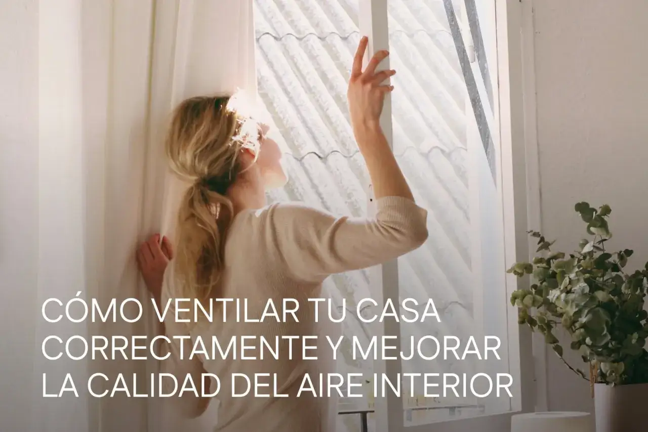Mujer abriendo ventana para mejorar la **calidad del aire interior**. La luz del sol ilumina su cabello rubio recogido.