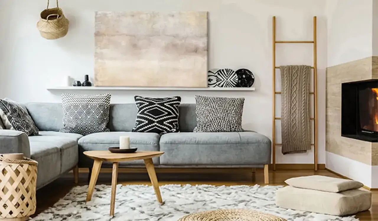 Un salon cosy avec un grand tableau beige abstrait au-dessus d'un canapé gris, des coussins graphiques et une cheminée.