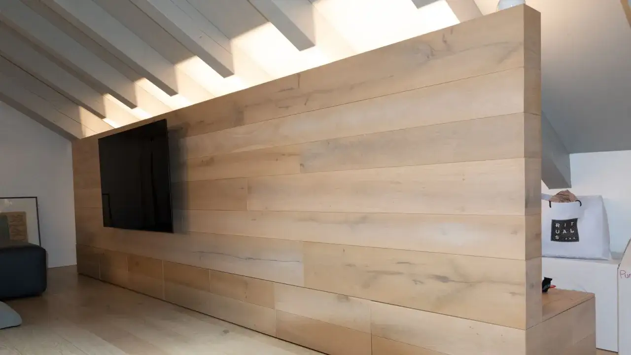 Parete in legno chiaro con TV a schermo piatto, dove la luce naturale prende luce dal tetto inclinato, creando un'atmosfera accogliente.
