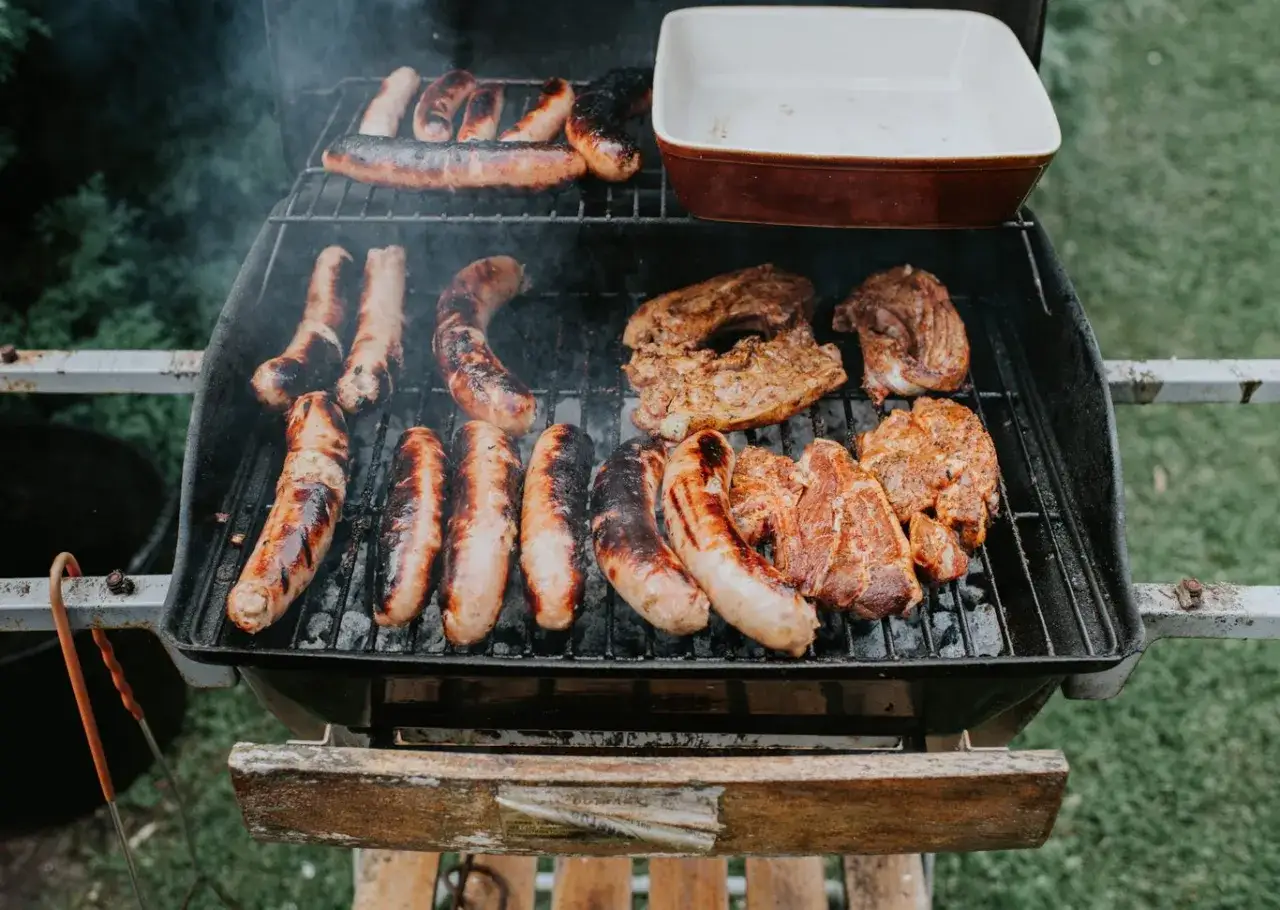 Saucisses et côtelettes grillent sur un barbecue. La différence charbon et charbon de bois est subtile, mais la saveur est bien réelle.