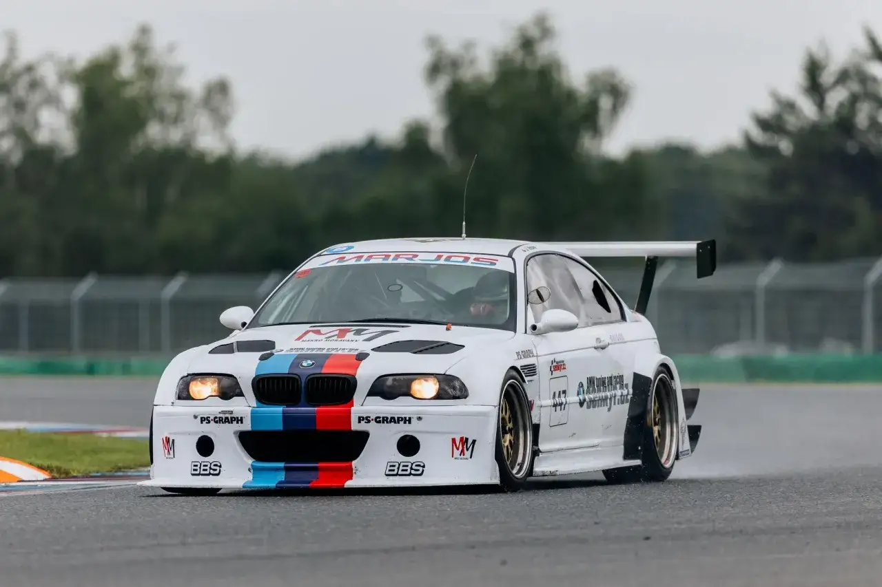 Białe BMW M3 GTR z kolorowymi pasami na masce i zderzaku, gotowe do wyścigu na torze.