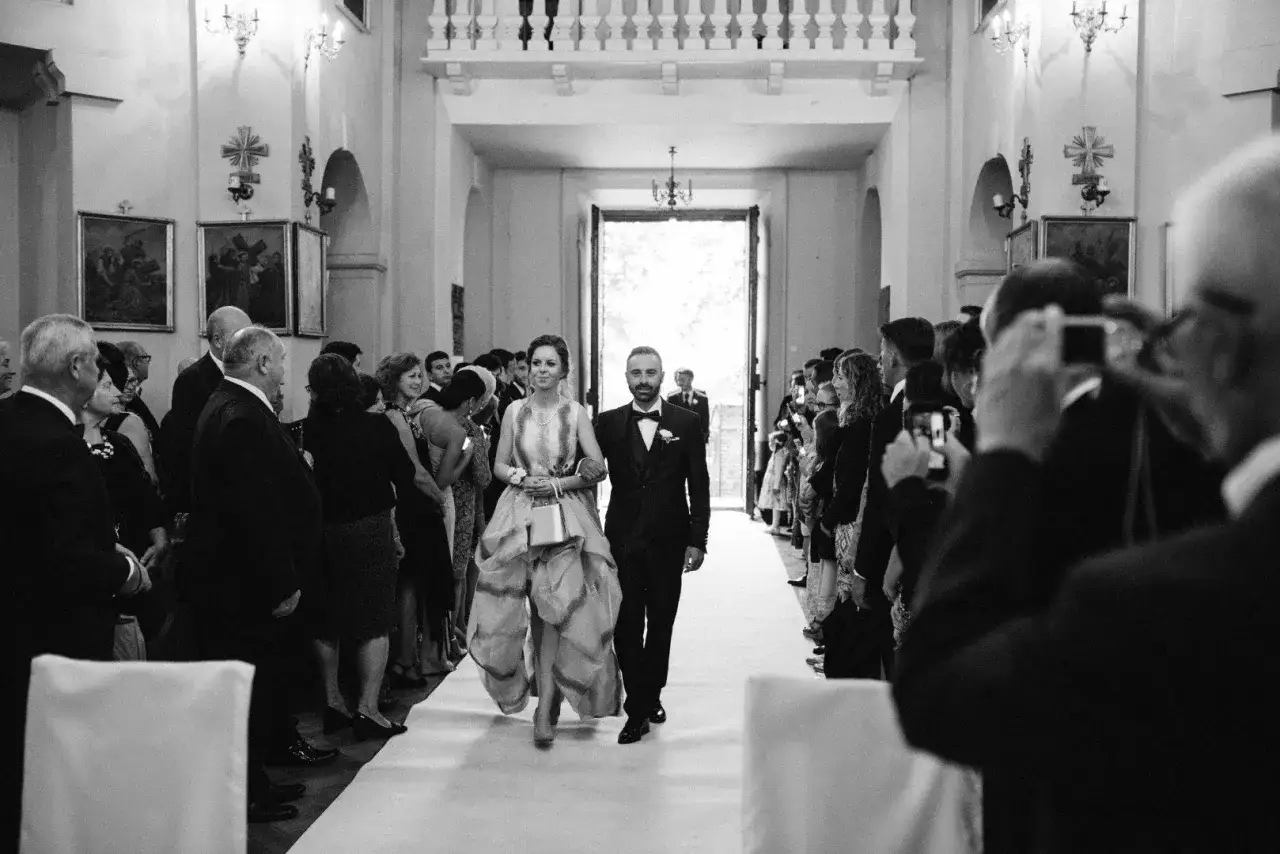 Para panny młodej idzie do ołtarza w kościele, otoczona gośćmi, kt&oacute;rzy robią zdjęcia.