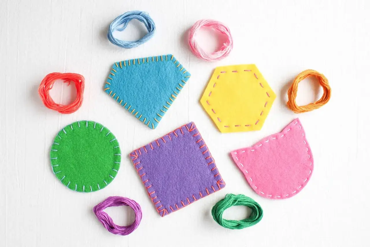 Posavasos de fieltro de colores, con formas geom&eacute;tricas y de gato, rodeados de hilos para coser.