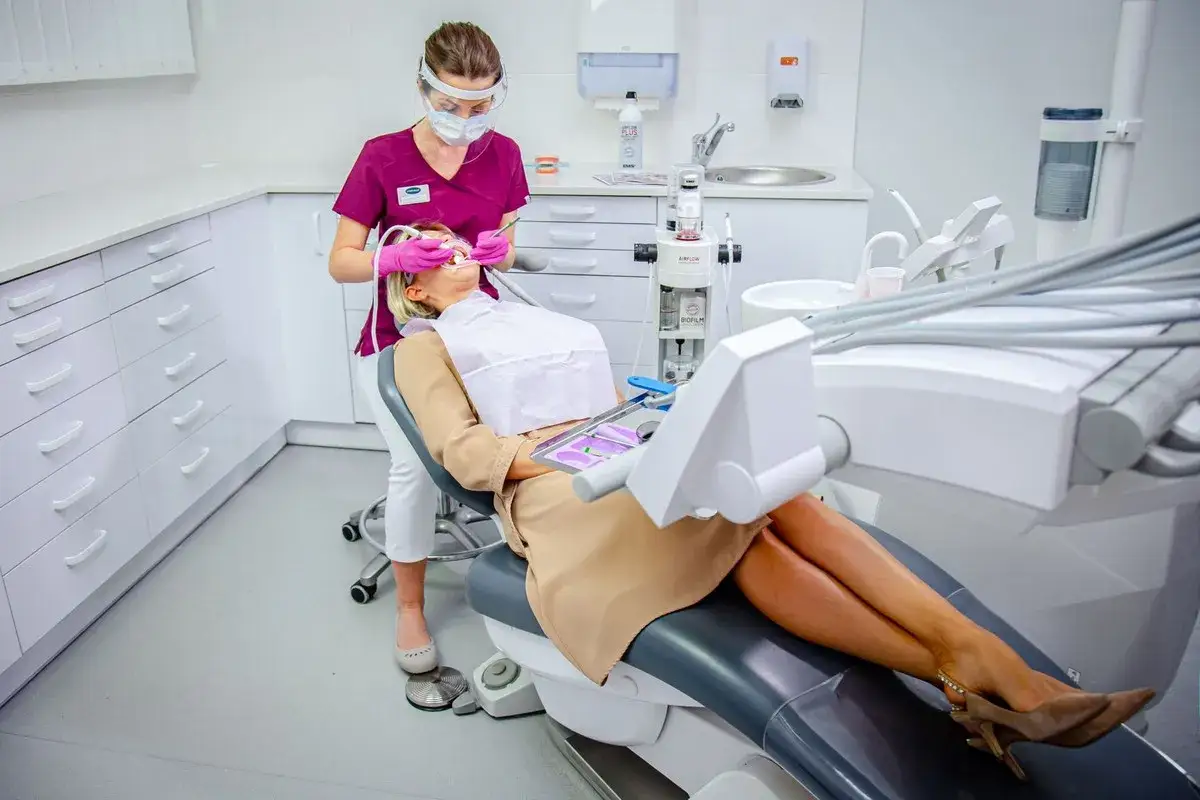 Stomatolog to lekarz, który dba o zdrowie Twoich zębów. W gabinecie stomatologicznym pacjentka siedzi na fotelu, a stomatolog w fartuchu i masce wykonuje zabieg.