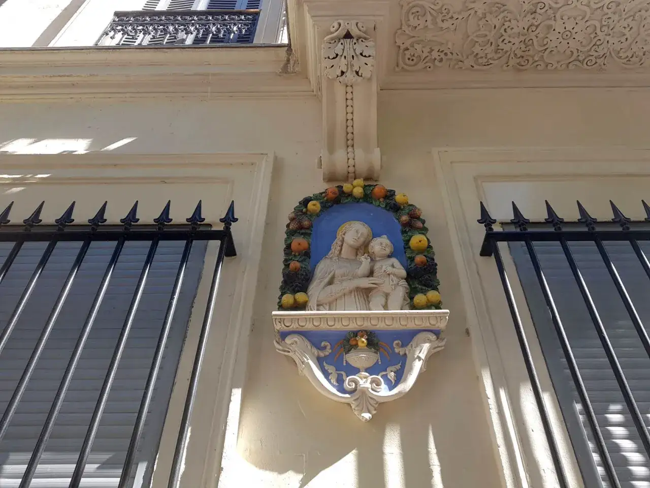 Vitraux d'une madone tenant son enfant, entour&eacute;e de fruits, sur une fa&ccedil;ade orn&eacute;e.
