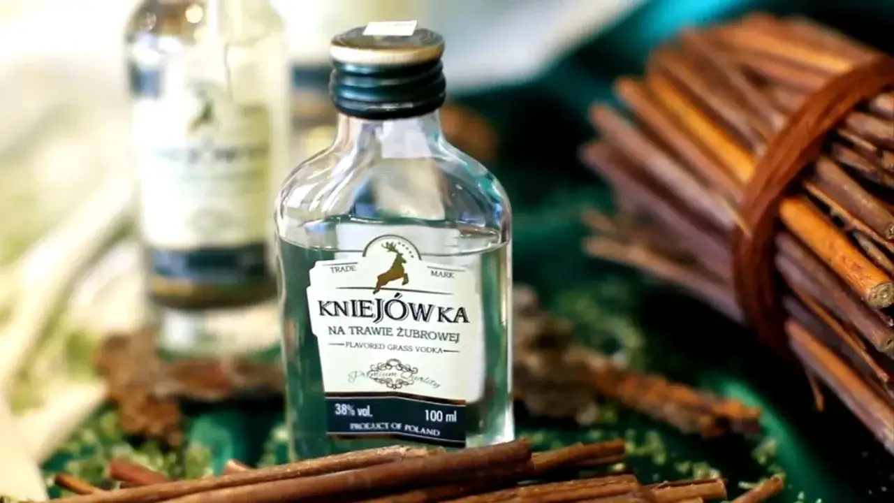 Miniaturka Kniejówki, idealny wybór, jaki alkohol na wesele. W tle inne butelki i laska cynamonu.