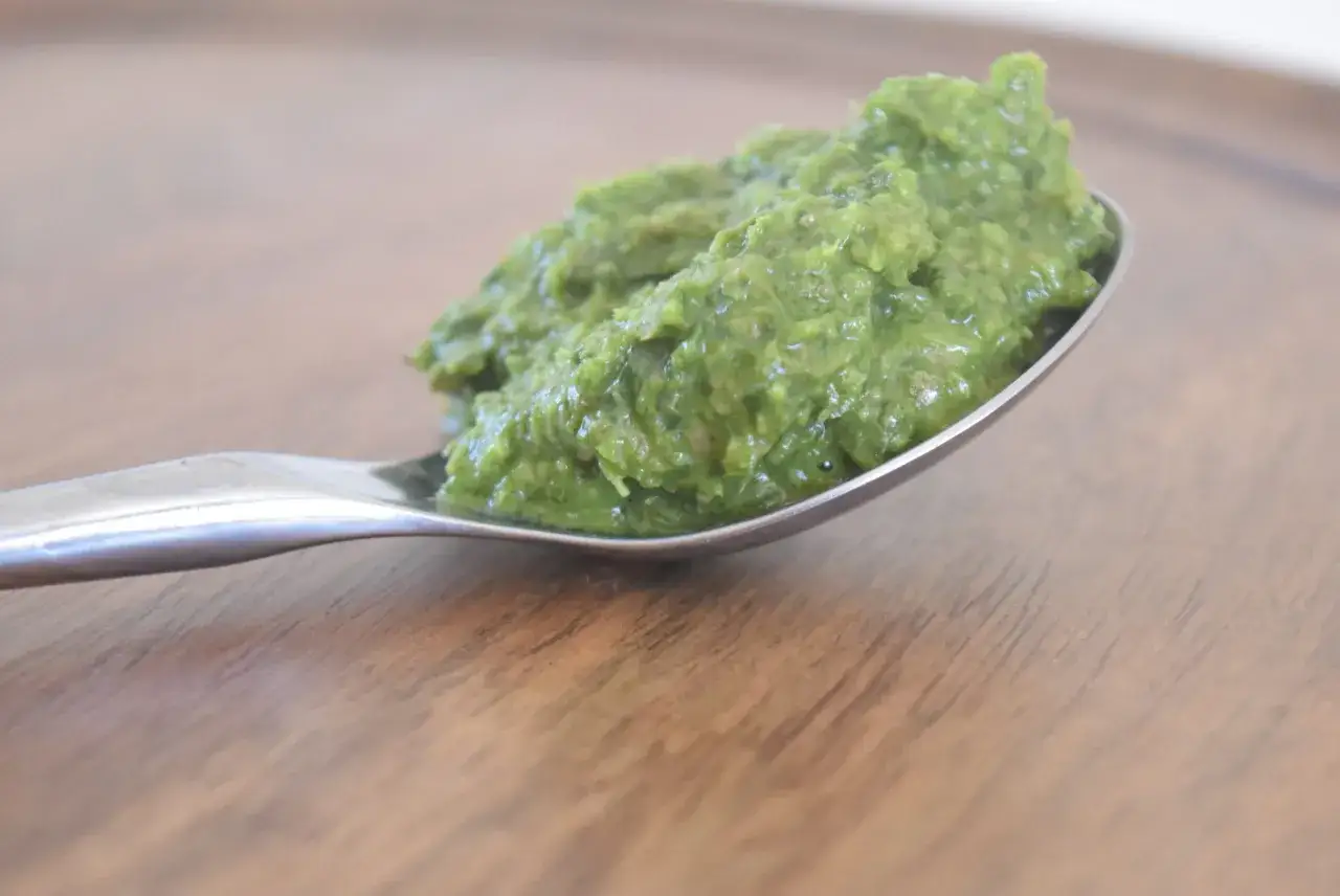 En sked med gr&ouml;n salsa verde, en h&auml;rlig &ouml;rtig s&aring;s, vilar p&aring; en tr&auml;yta.