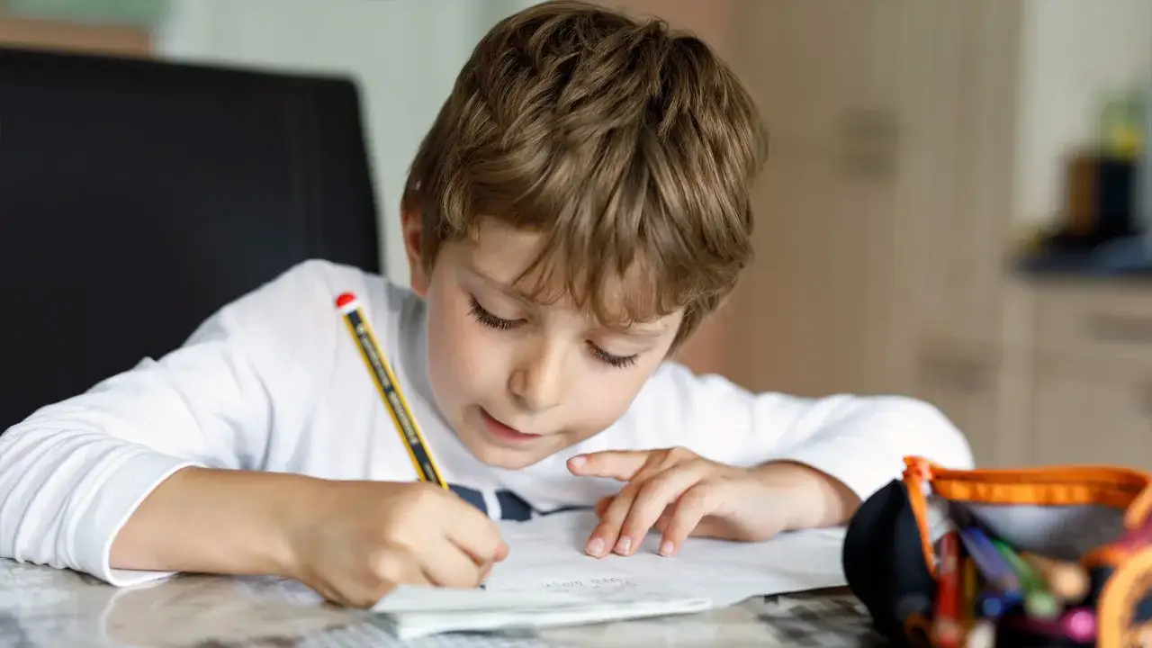 Ni&ntilde;o concentrado resolviendo problemas 4 primaria. L&aacute;piz en mano, cuaderno abierto y estuche de colores cerca.