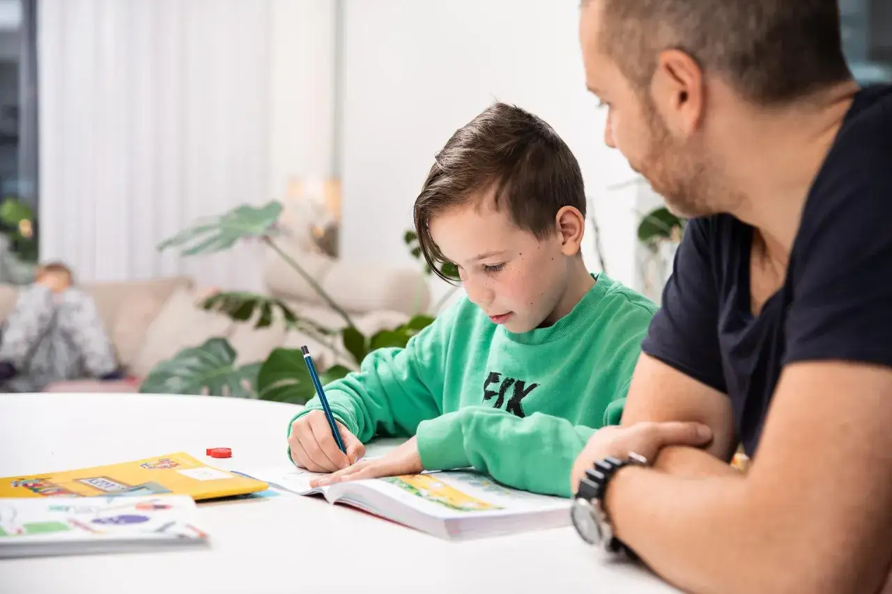 Pojke med fr&auml;knar koncentrerar sig p&aring; l&auml;xor, en pappa tittar p&aring;. Kan vara tidiga tecken p&aring; adhd.
