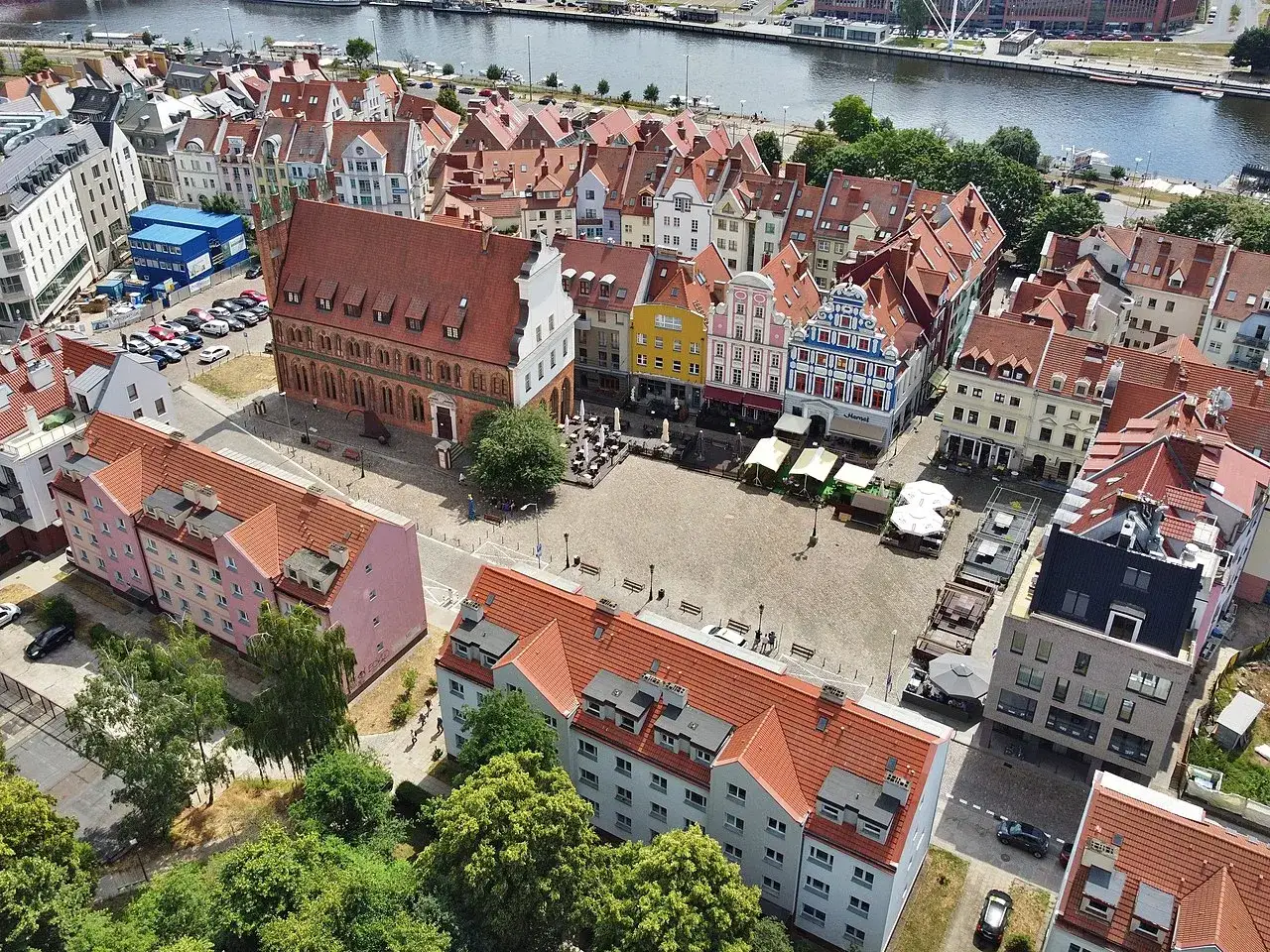Widok z lotu ptaka na kolorowy rynek w Szczecinie, z kamienicami, rzeką i zielenią.