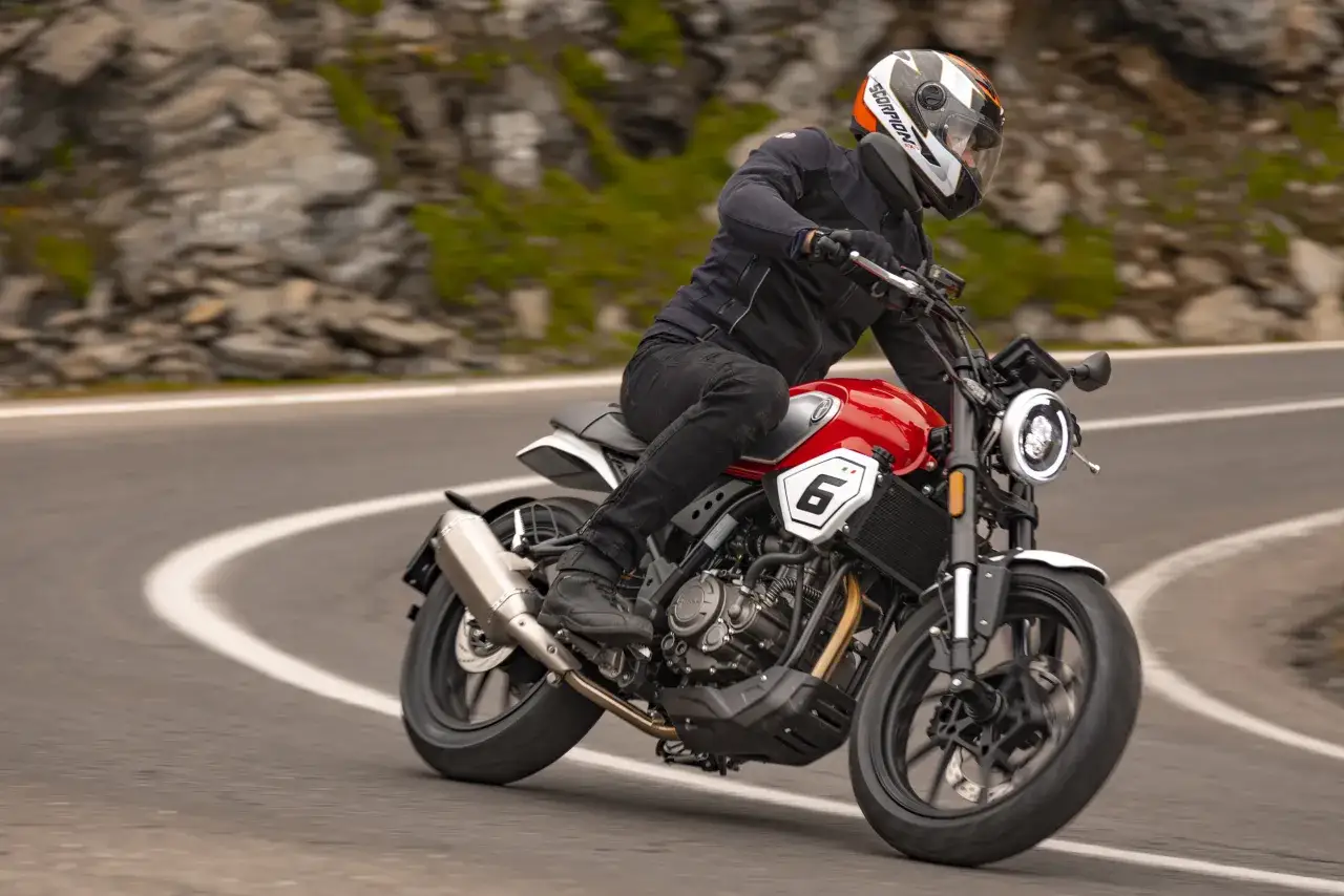 Motocyklista w kasku jedzie na czerwonym Junak SC 125 V Max po krętej drodze wśród skalistych zboczy.