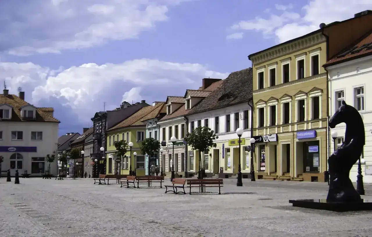 Konin atrakcje: Rynek z kamienicami i rzeźbą konia. Ławki zapraszają do odpoczynku w słoneczny dzień.