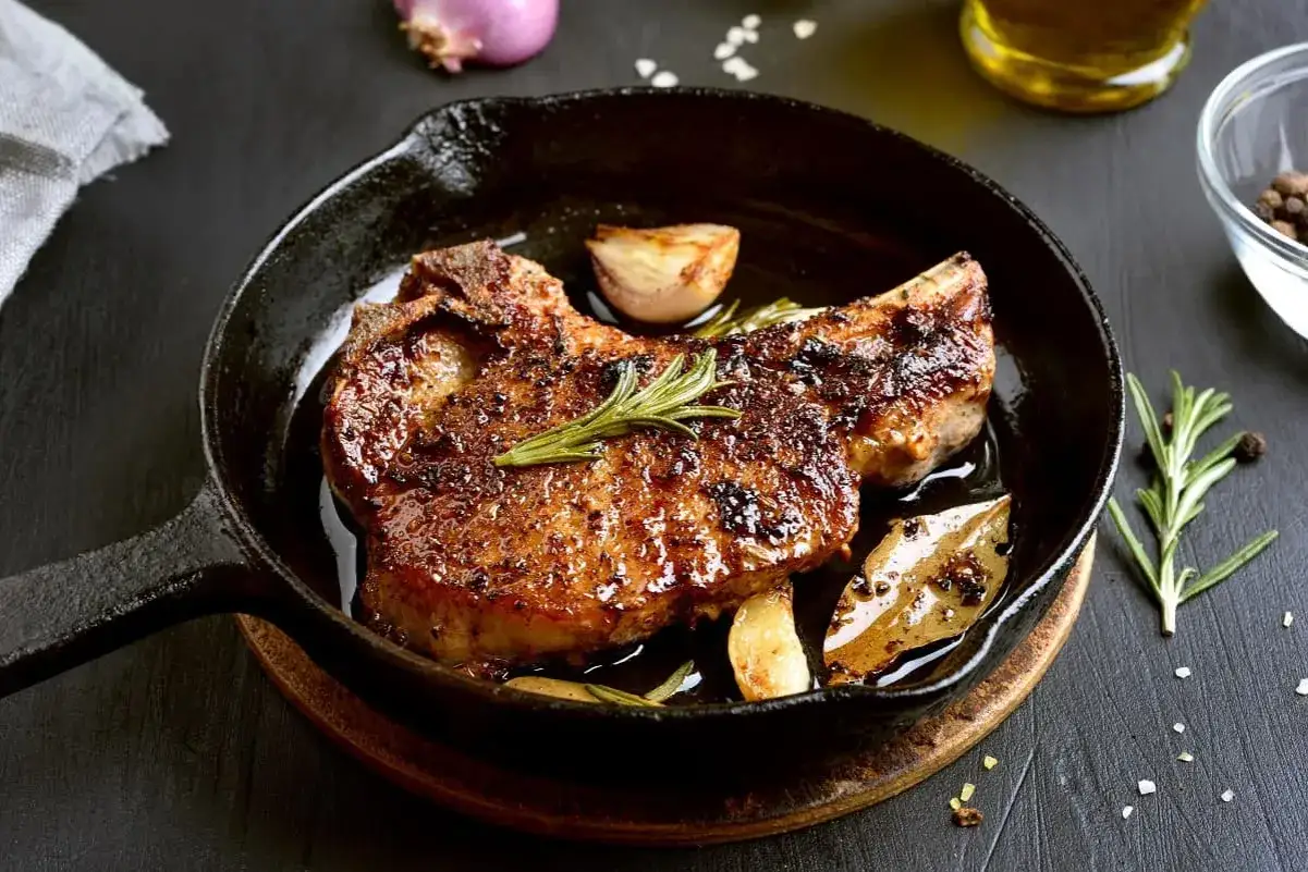 Chuleta de ternera al horno, jugosa y dorada, servida en sart&eacute;n de hierro fundido con ajo, romero y laurel.