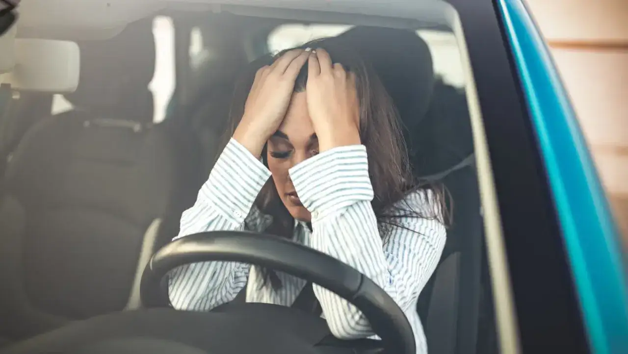Frau mit H&auml;nden auf dem Kopf im Auto, k&auml;mpft mit Angst vorm Autofahren.