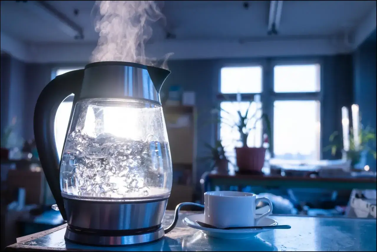Une bouilloire en verre fait bouillir de l'eau chaude, avec de la vapeur s'élevant. Une tasse à café est prête à être remplie.