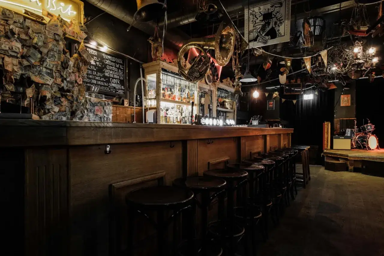 En bar i Stockholm med en vägg täckt av sedlar, instrument i taket och en scen med trummor.