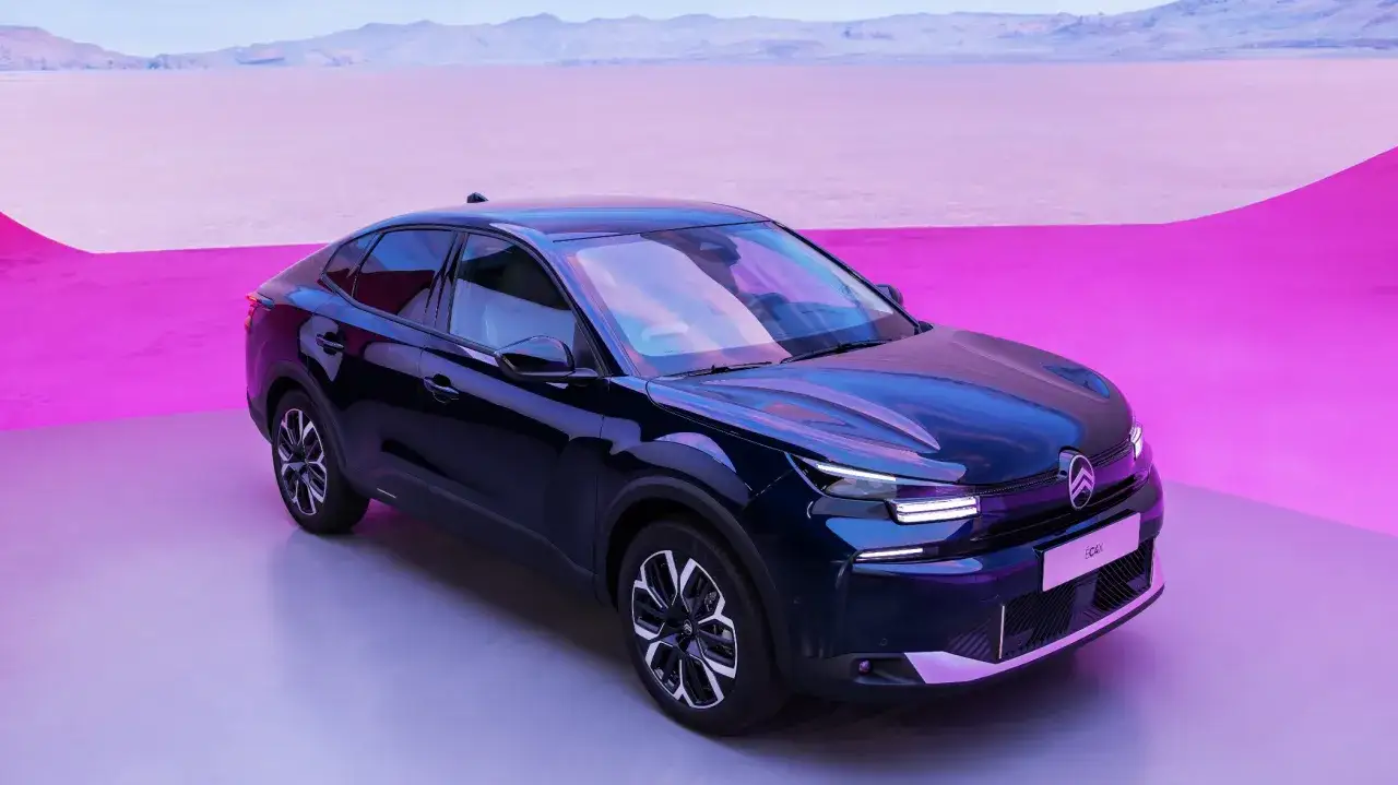 Mörkblå Citroën C4 elbil står på en ljusgrå yta med en rosa bakgrund och berg i fjärran.