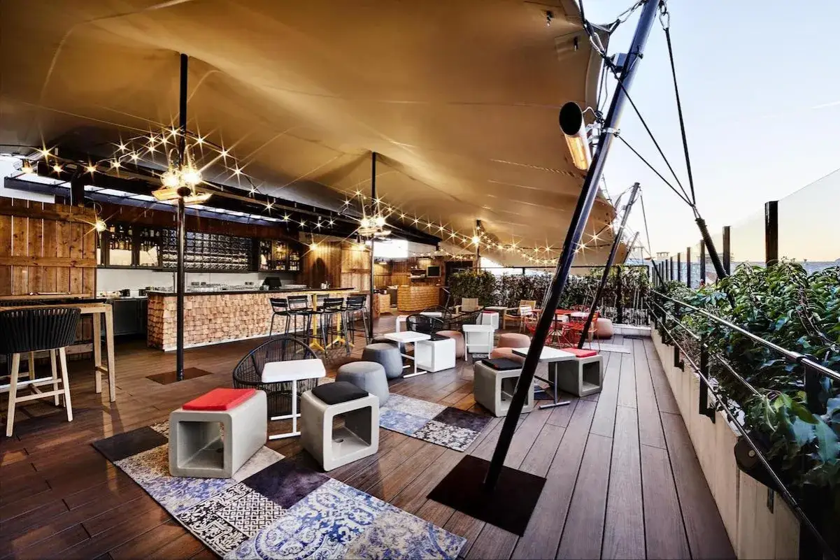 Ambiance chaleureuse sur un rooftop Paris pas cher, avec bar en bois, lumières festives et sièges confortables.