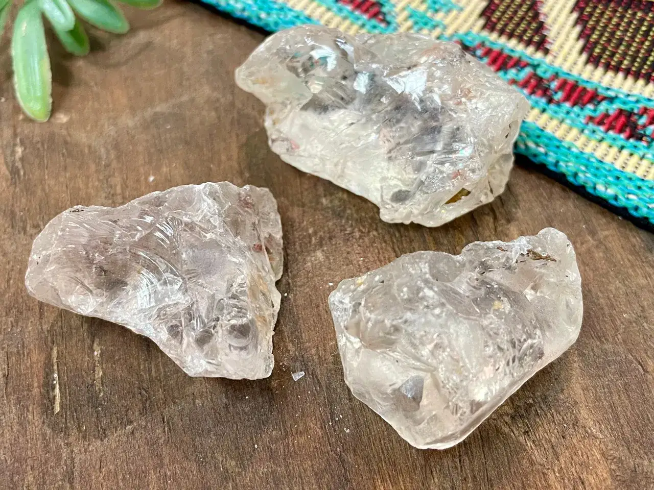 Tres fragmentos de cristal de roca, mostrando sus propiedades de claridad y textura natural sobre una superficie de madera.