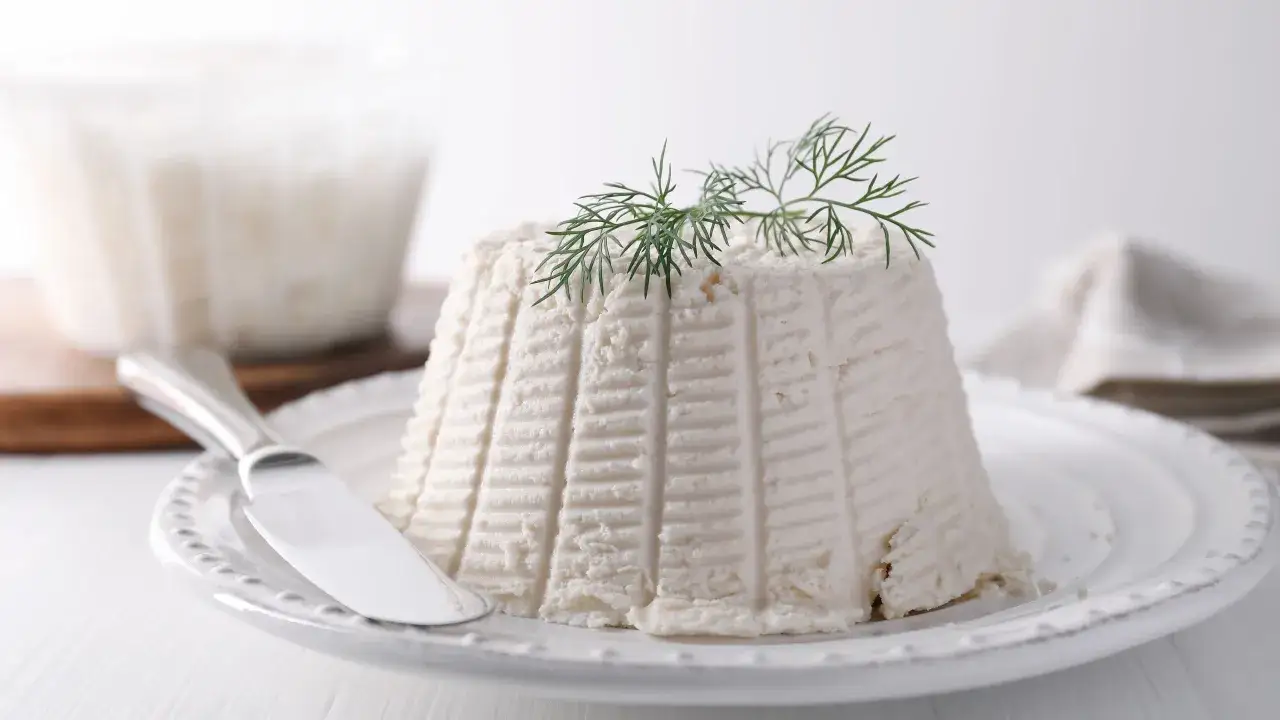 Ricotta fresca su piatto bianco, guarnita con aneto. La sua consistenza soffice rivela cosa contiene la ricotta: latte e siero.