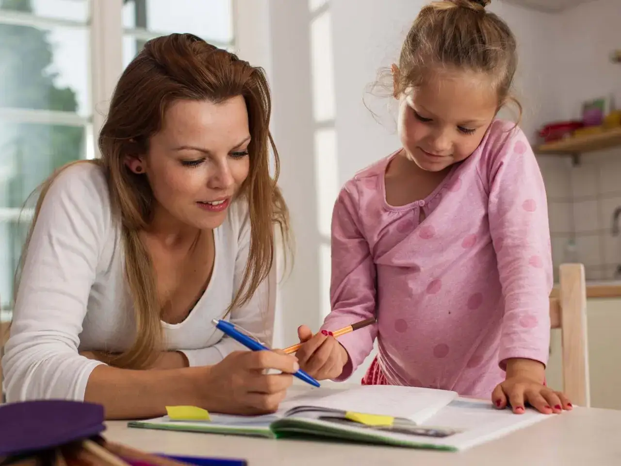 Donna aiuta bambina con i compiti vacanze estive, concentrati su un quaderno aperto.