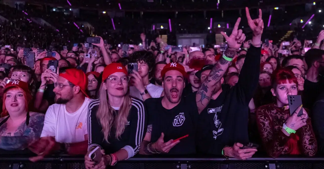 Tłum na **impact festival** z telefonami w górze, niektórzy pozdrawiają gestem rockowego rogu.